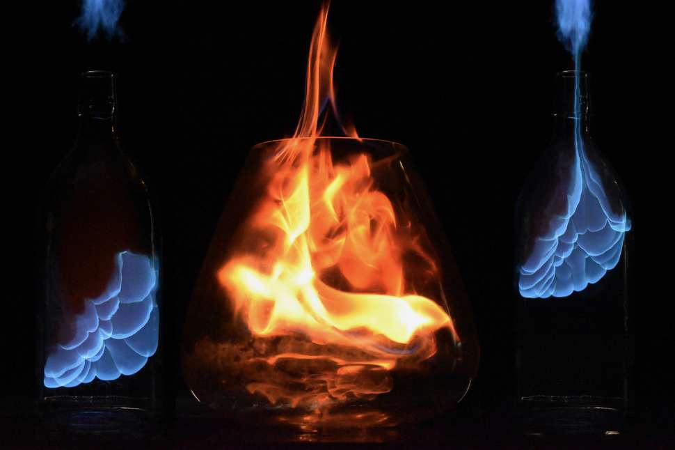 An artistic photo of a flame in a glass flanked by two bottles with blue flame inside