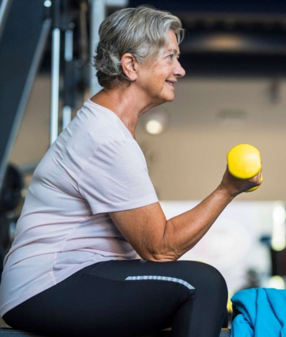 Older lady smiling and lifting yellow weight