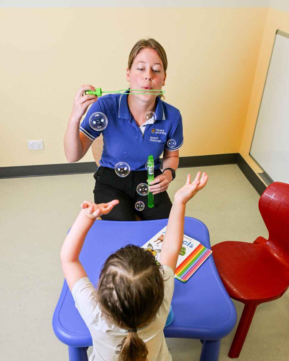 Flinders Speech Pathology Student blowing bubbles with young girl trying to pop them