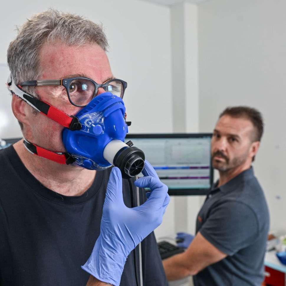 Man with mask on for exercise testing with clinician stood behind him