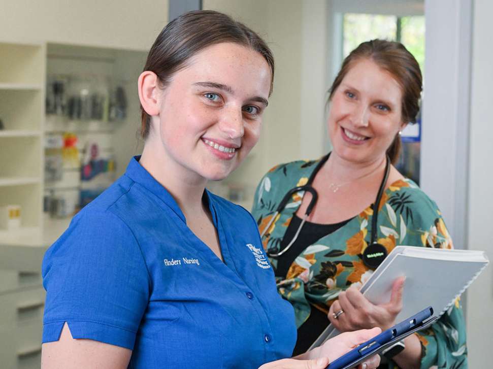 Flinders Nursing Student smiling and holding ipad with nurse stood behind her