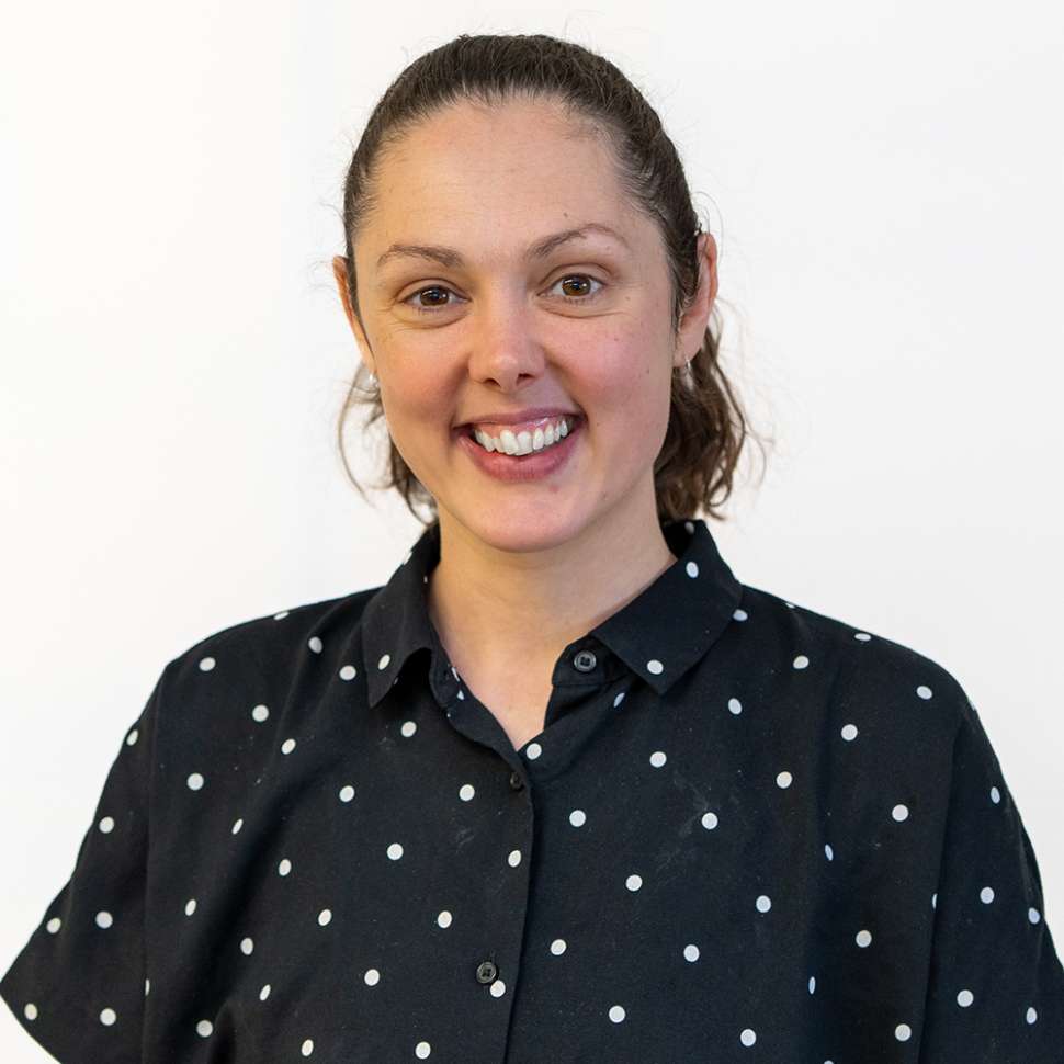Smiling woman with a black dotted shirt behind a white backdrop