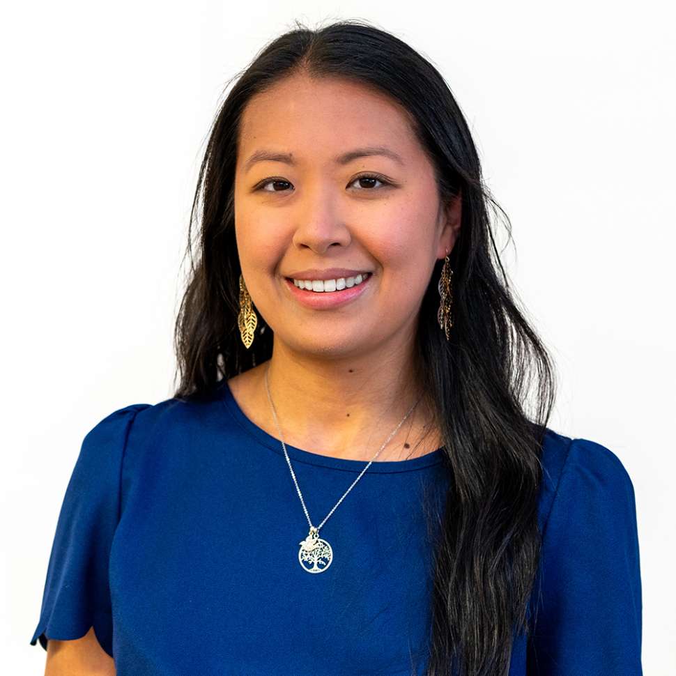Smiling woman with a blue top behind a white backdrop
