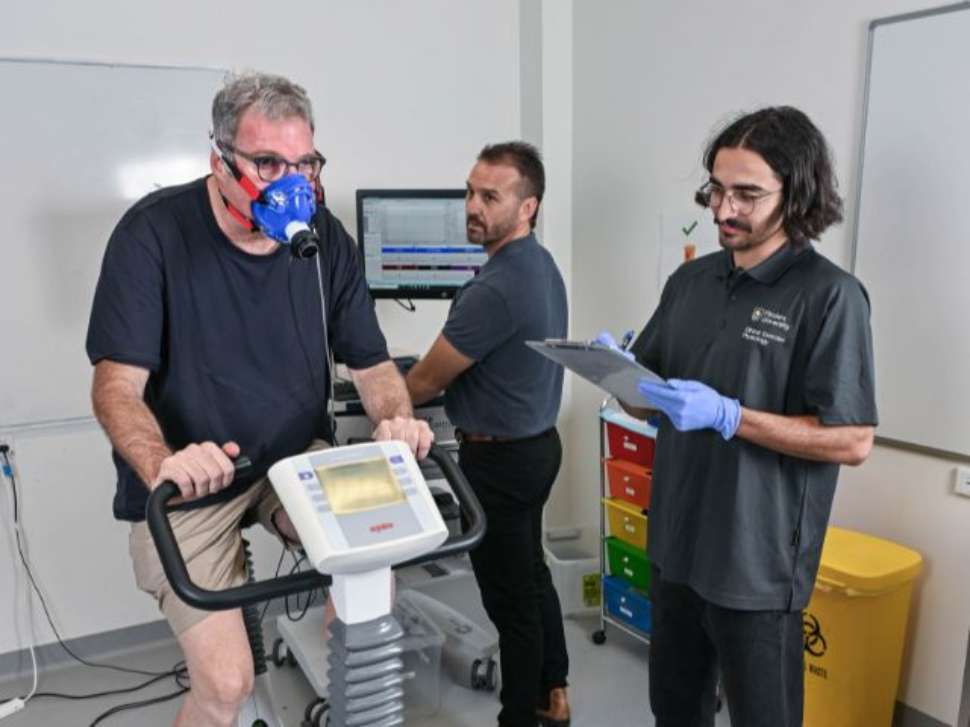 Man on exercise bike doing testing with a mask on with flinders exercise physiology student and teacher next to him