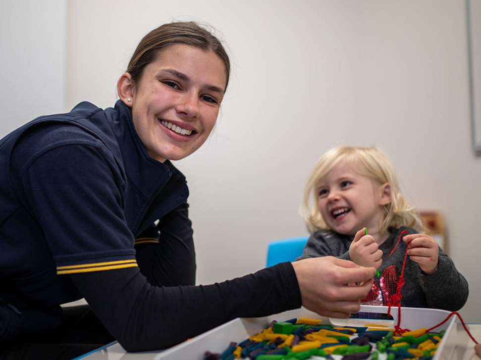 Flinders Occupational Therapist smiling at camera with child smiling and playing next to her