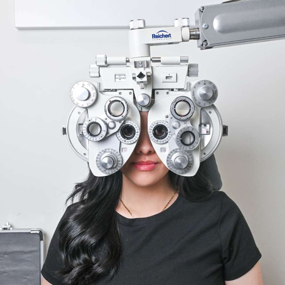 Woman sitting in eye exam room, with testing equipment in front of eyes