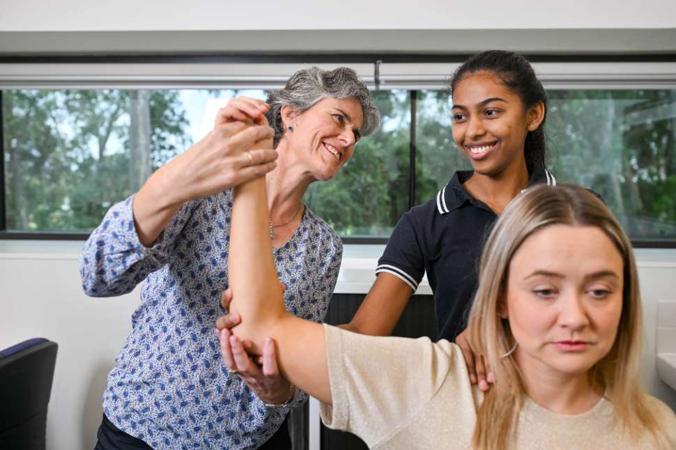 Flinders Physiotherapy Student with clinician holding up patient's arm and smiling