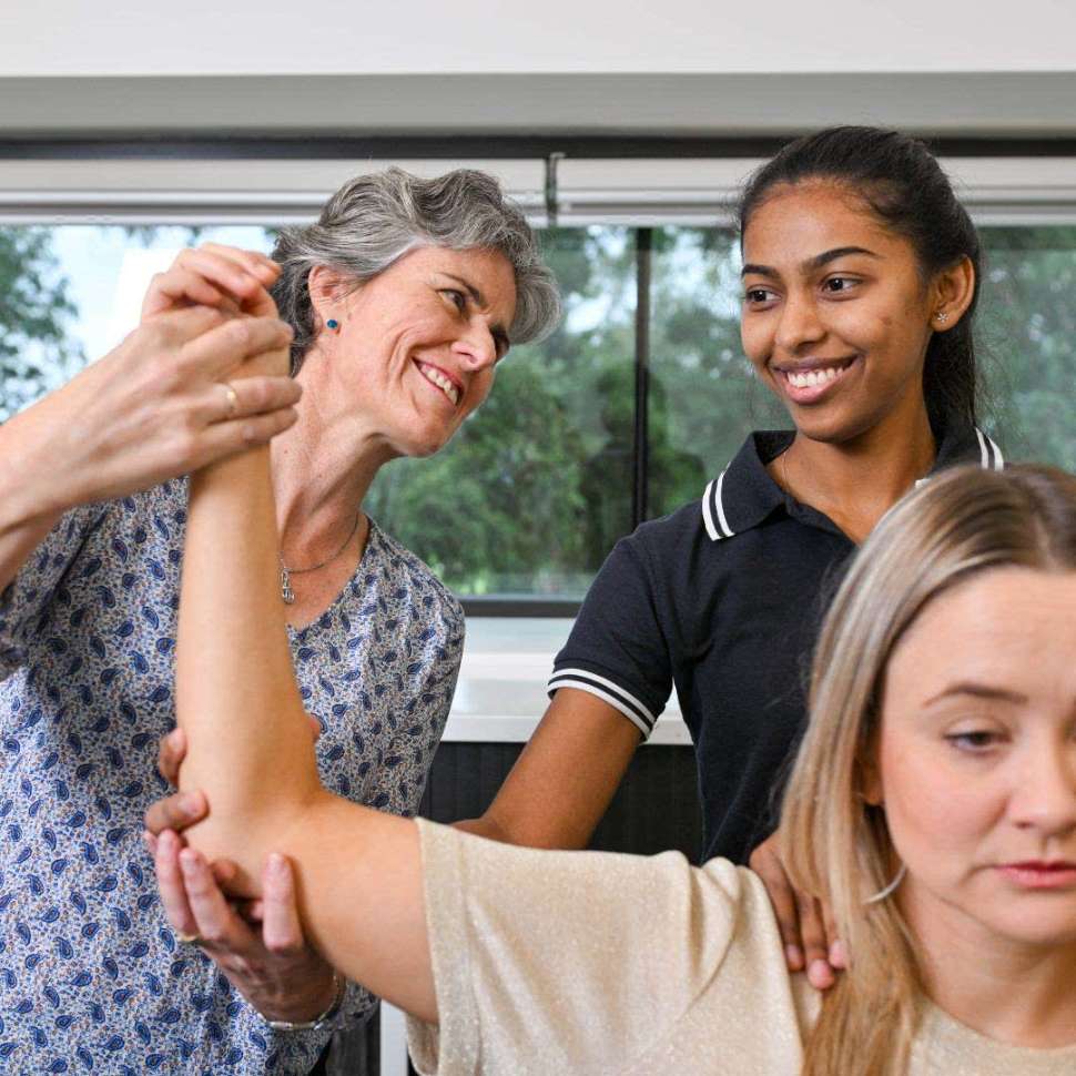 Flinders Physiotherapy Student with clinician holding up patient's arm and smiling