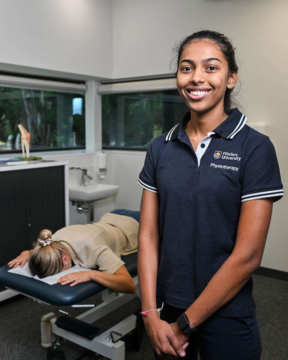 Flinders Physiotherapy Student smiling at camera with patient lying on bed in background