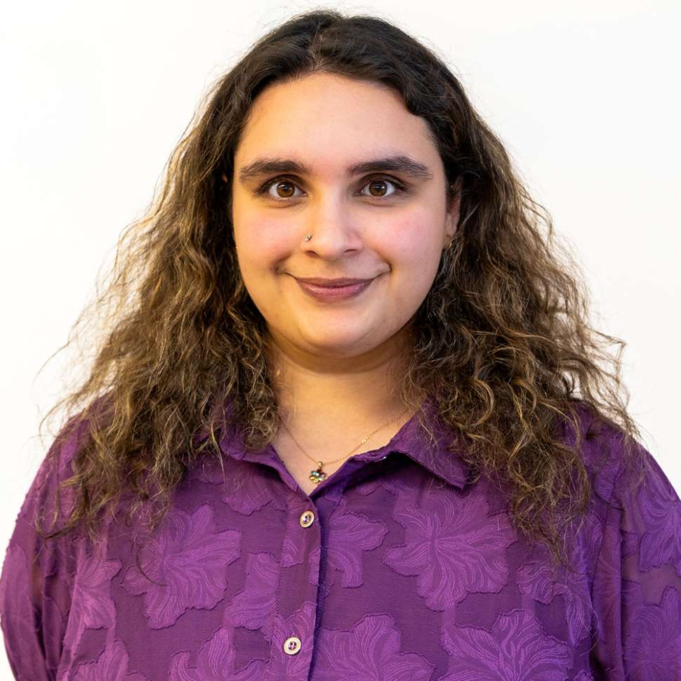 Smiling woman with a purple floral shirt behind a white backdrop