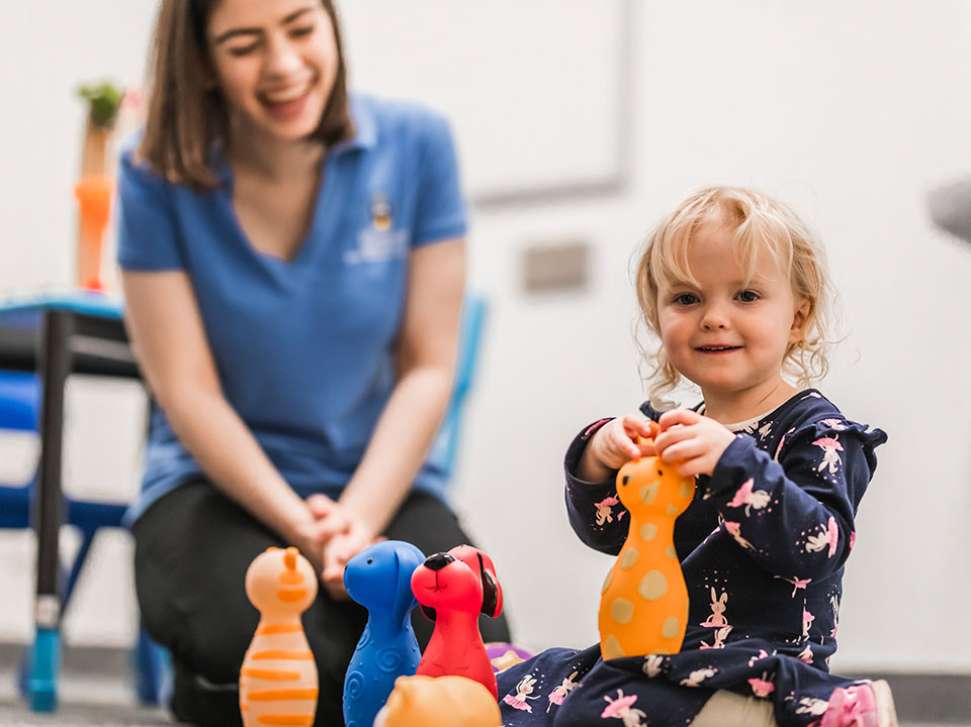 Flinders Speech Pathology Student playing with young child, both smiling with toys in front