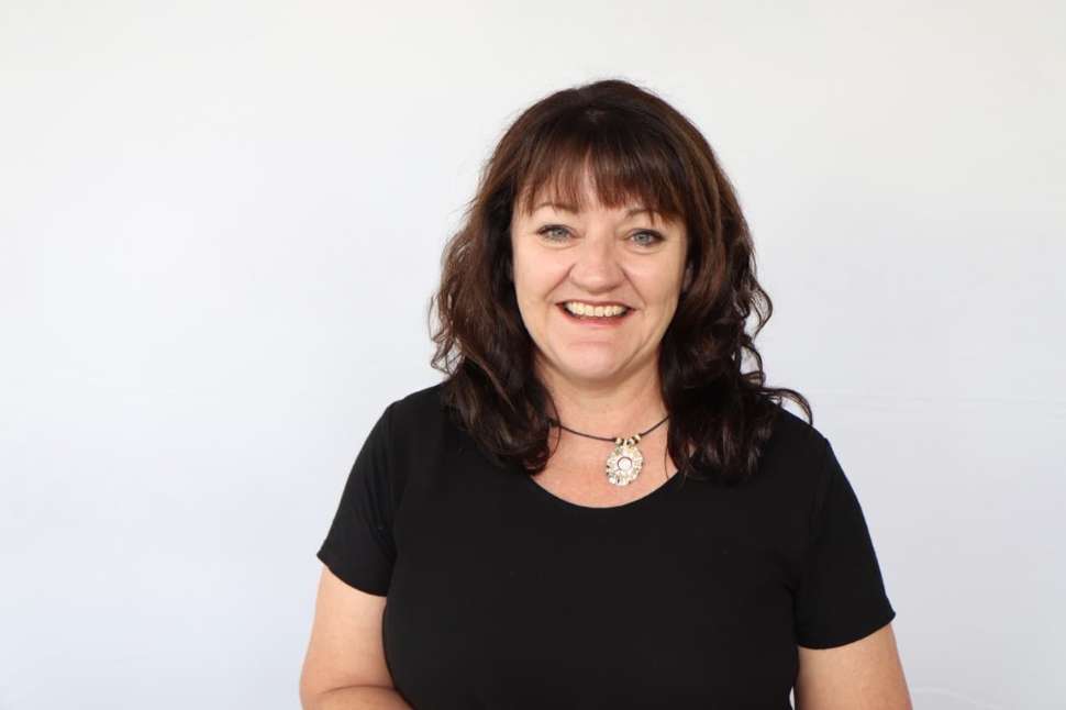 Smiling woman in a black top standing in front of a Flinders University branded backdrop.
