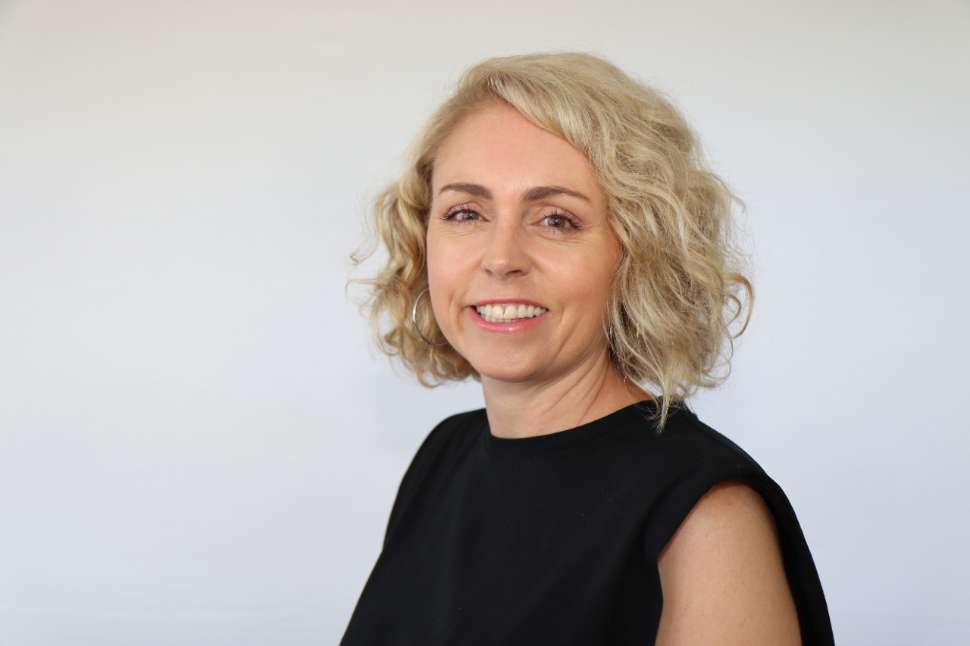 Smiling woman in a black top standing in front of a Flinders University branded backdrop.