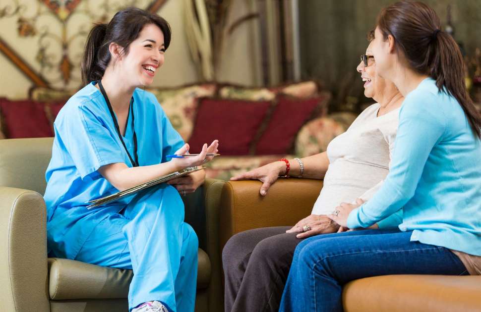 A nurse speaks to two patients sitting on a couch
